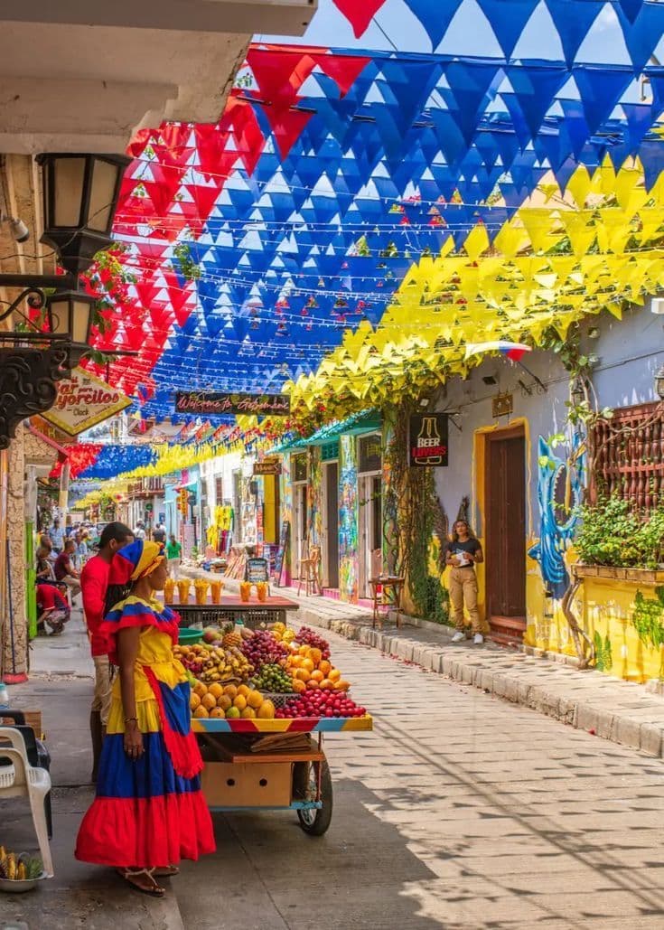 Calle colorida con vendedora de frutas y banderas de Colombia en Cartagena de Indias — paquete desde Chile